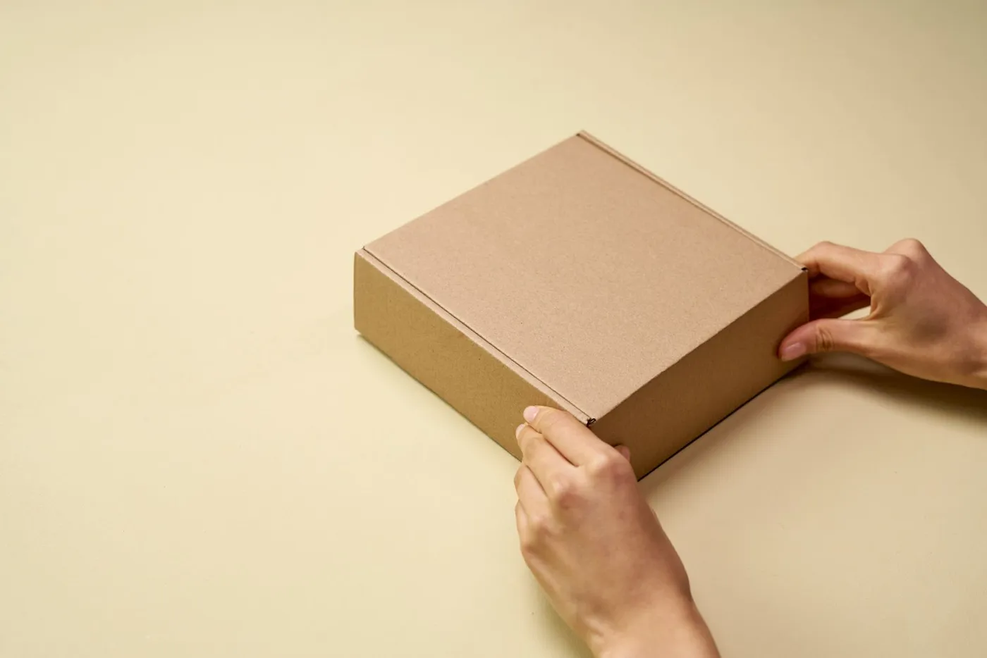 Two hands setting down a closed cardboard shipping box.