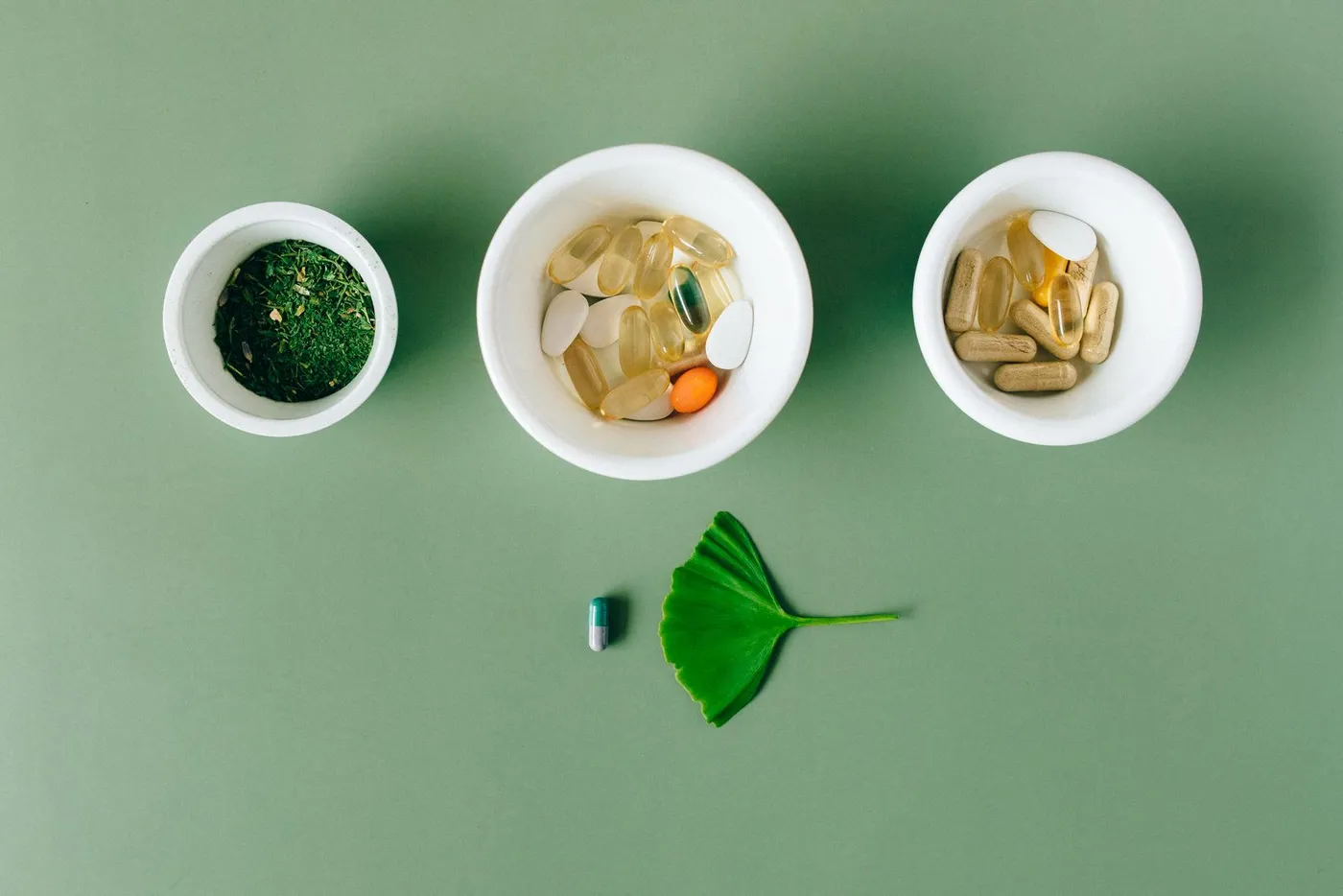 Three white bowls of capsules and powder on a green surface.